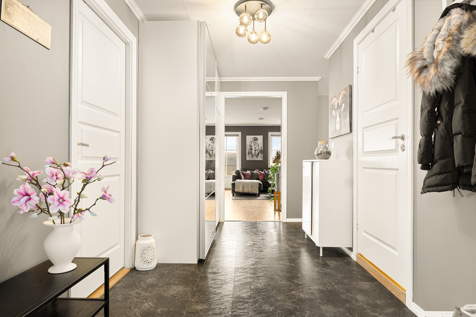 Entré med lyse overflater, laminatfliser på gulv og praktisk skyvedørsgarderobe. Galleribilde