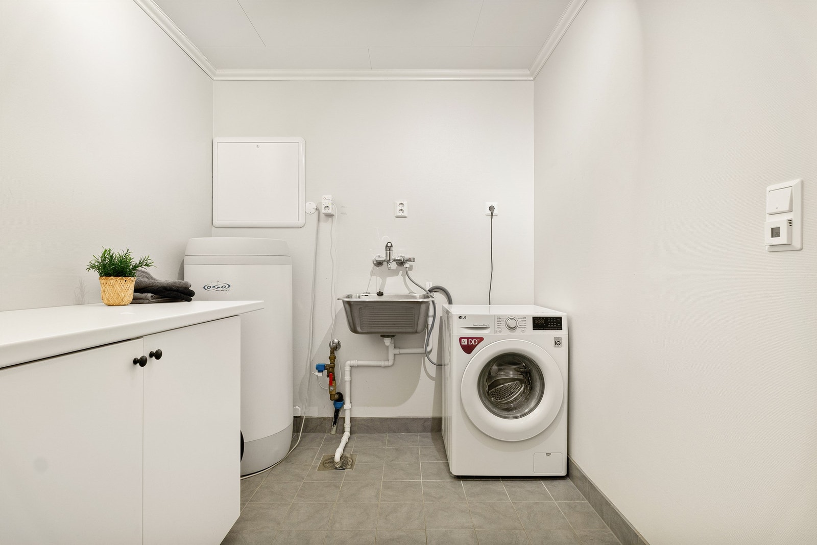 Stort og praktisk vaskerom i u. etasje med fliser på gulv og gulvvarme. Utstyrt med varmtvannsbereder, utslagsvask og skapinnredning. Sentral for rør-i-rør er plassert her. Galleribilde