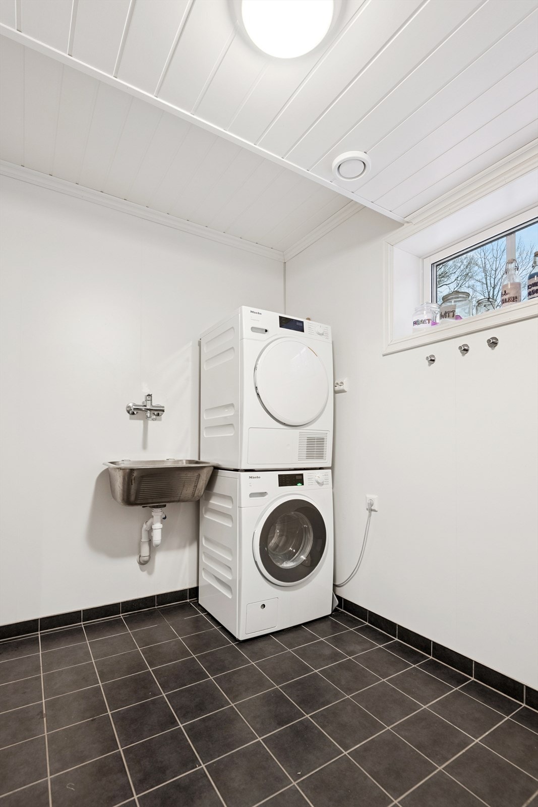 Separat vaskerom med flislagt gulv, utslagskum og opplegg for vaskemaskin. Galleribilde