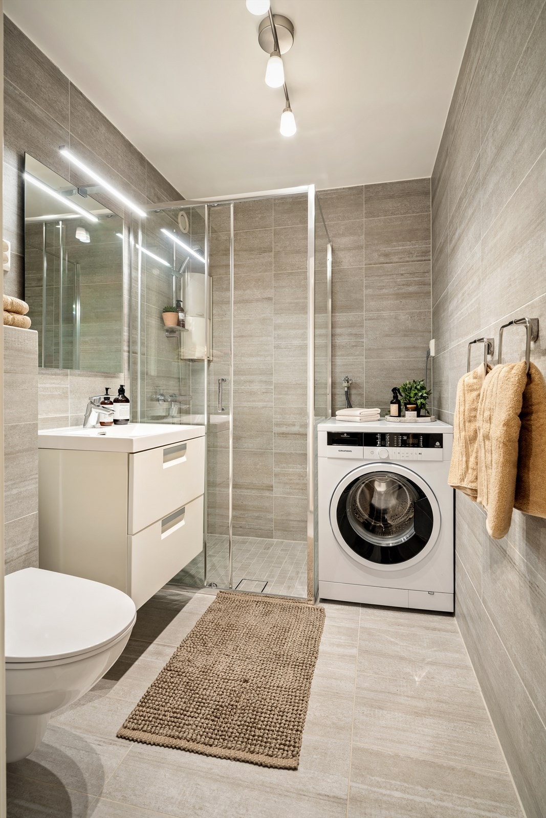 Baderommet er innredet med nedfelt servant, veggmontert toalett, dusjvegger/hjørne og opplegg for vaskemaskin. Galleribilde