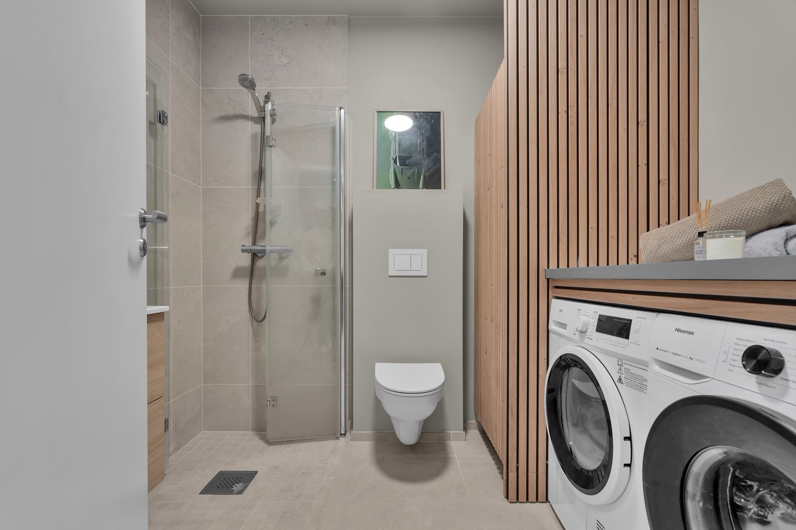 I 1. etasje finner du et praktisk bad kombinert med vaskerom. Her er det fliser på gulvet og varmekabler som gir en lun og komfortabel opplevelse. Veggene er slette og malt i en moderne farge som gir rommet et friskt og tidløst uttrykk. Galleribilde