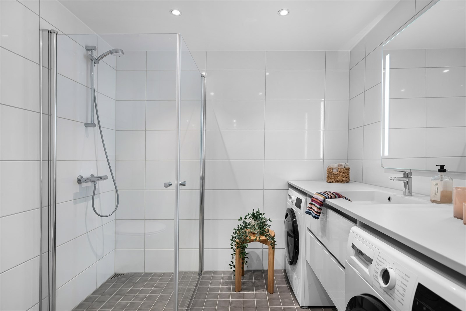 Rommet er godt utnyttet og har belysning fra downlights. Langs hele den ene langveggen er det baderomsinnredning med plass for både vaskemaskin og tørketrommel. Galleribilde