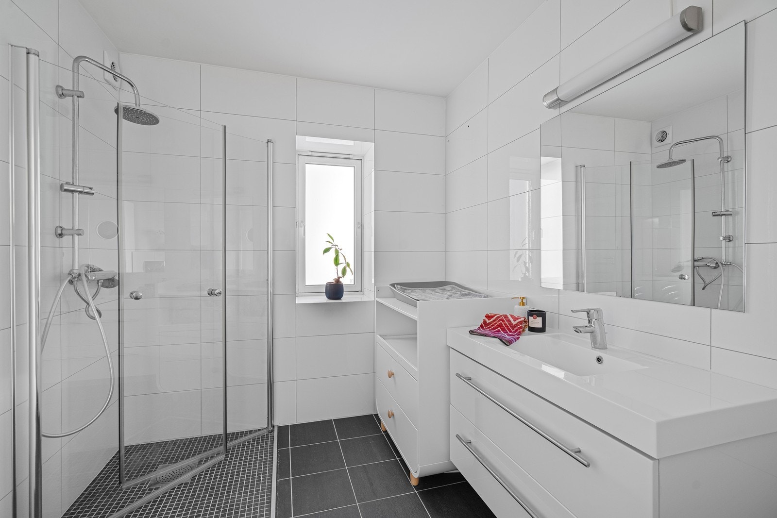 Badet i hovedetasjen har fliser på gulv og vegg, nedfelt vask i skuffeseksjon, dusj og vegghengt toalett. Galleribilde