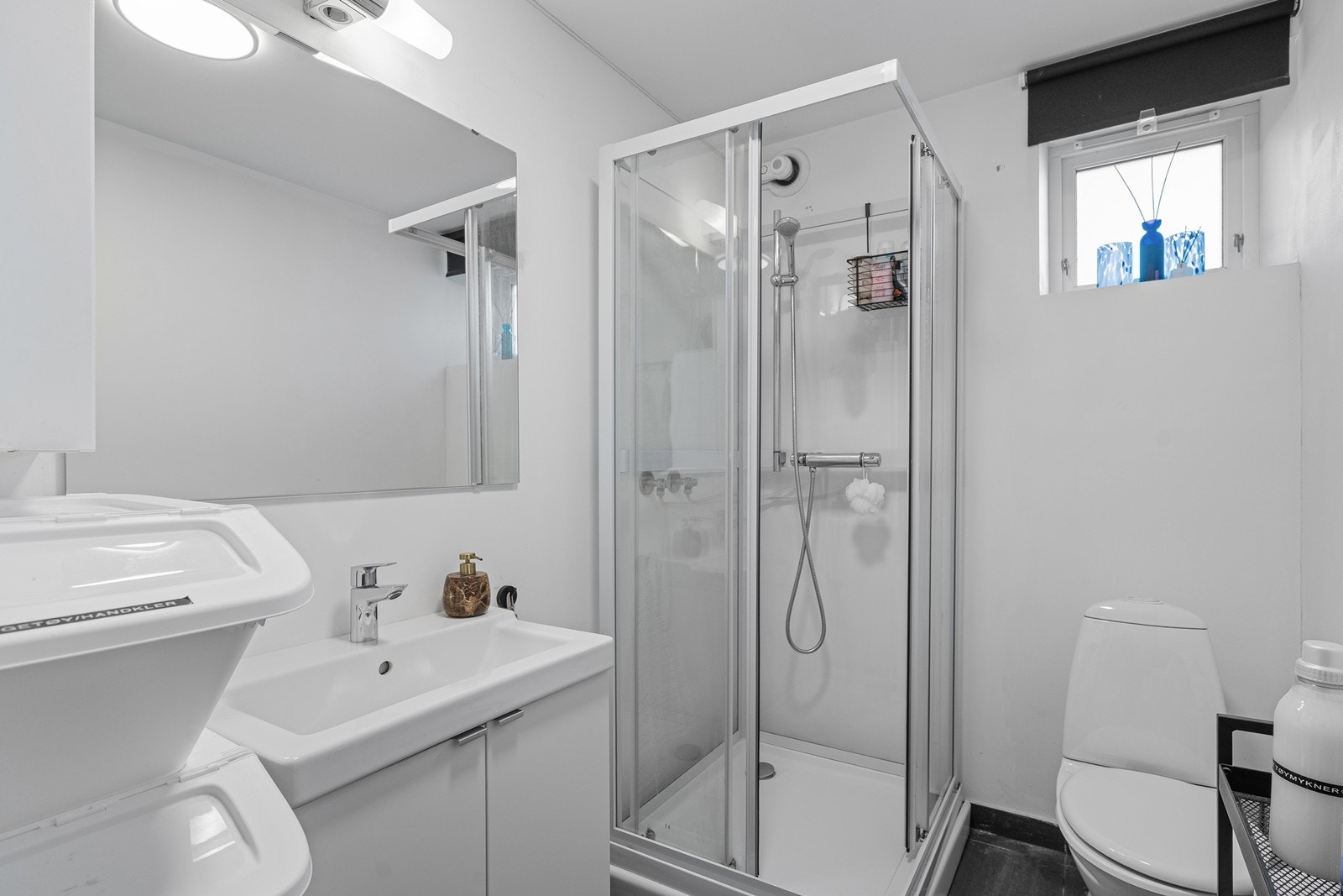 Bad i kjeller med dusjkabinett, toalett og servant i skapseksjon. Galleribilde