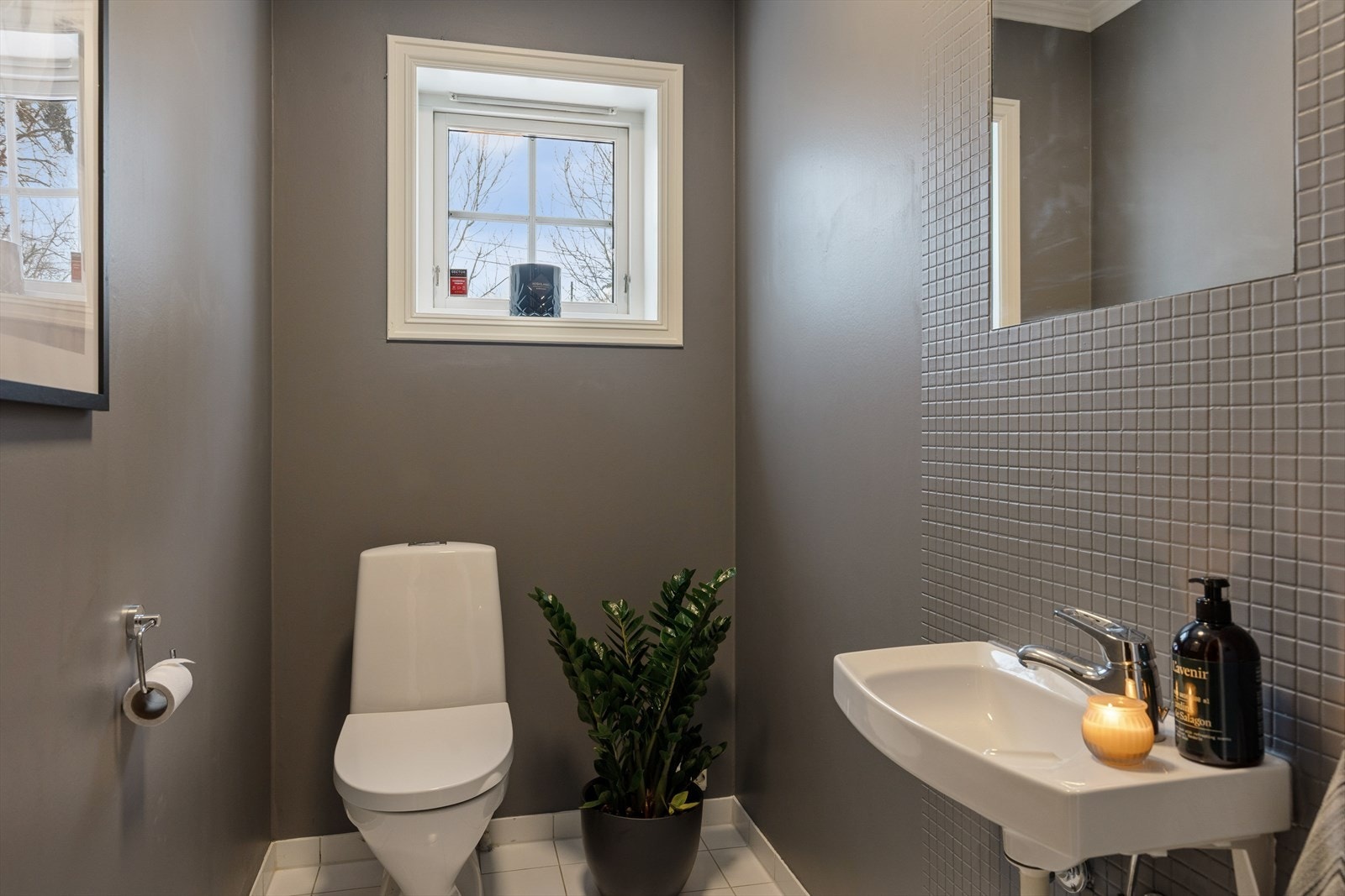 Toalettrom med fliser på gulv og malte vegger. Rommet har frittstående toalett og vegghengt vask. Galleribilde