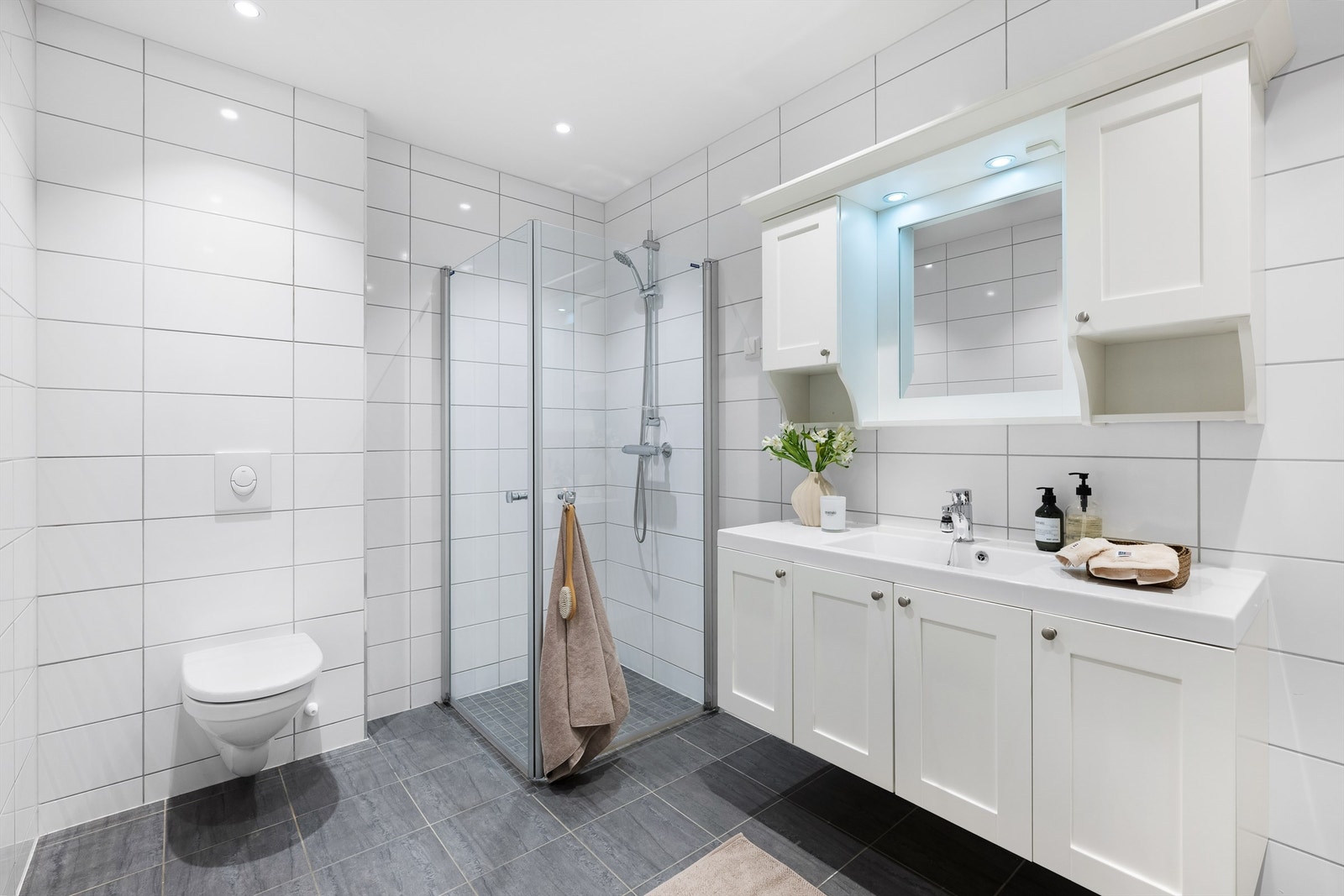 Helfliset baderom med gulvvarme som er innredet med vegghengt wc, dusjhjørne og baderomsmøbler Galleribilde