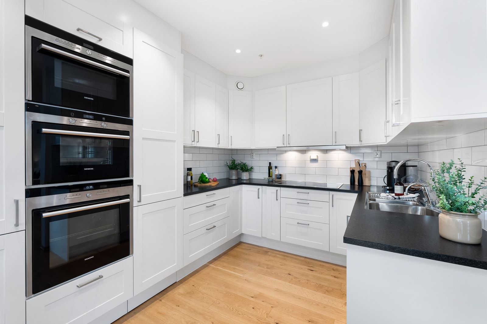 Innholdsrik kjøkkeninnredning med benkeplate i laminat og fliser mellom kjøkkenbenk og overskap. Praktisk med 2 stekeovner og mikro i kvalitetsmerke Siemens. Galleribilde