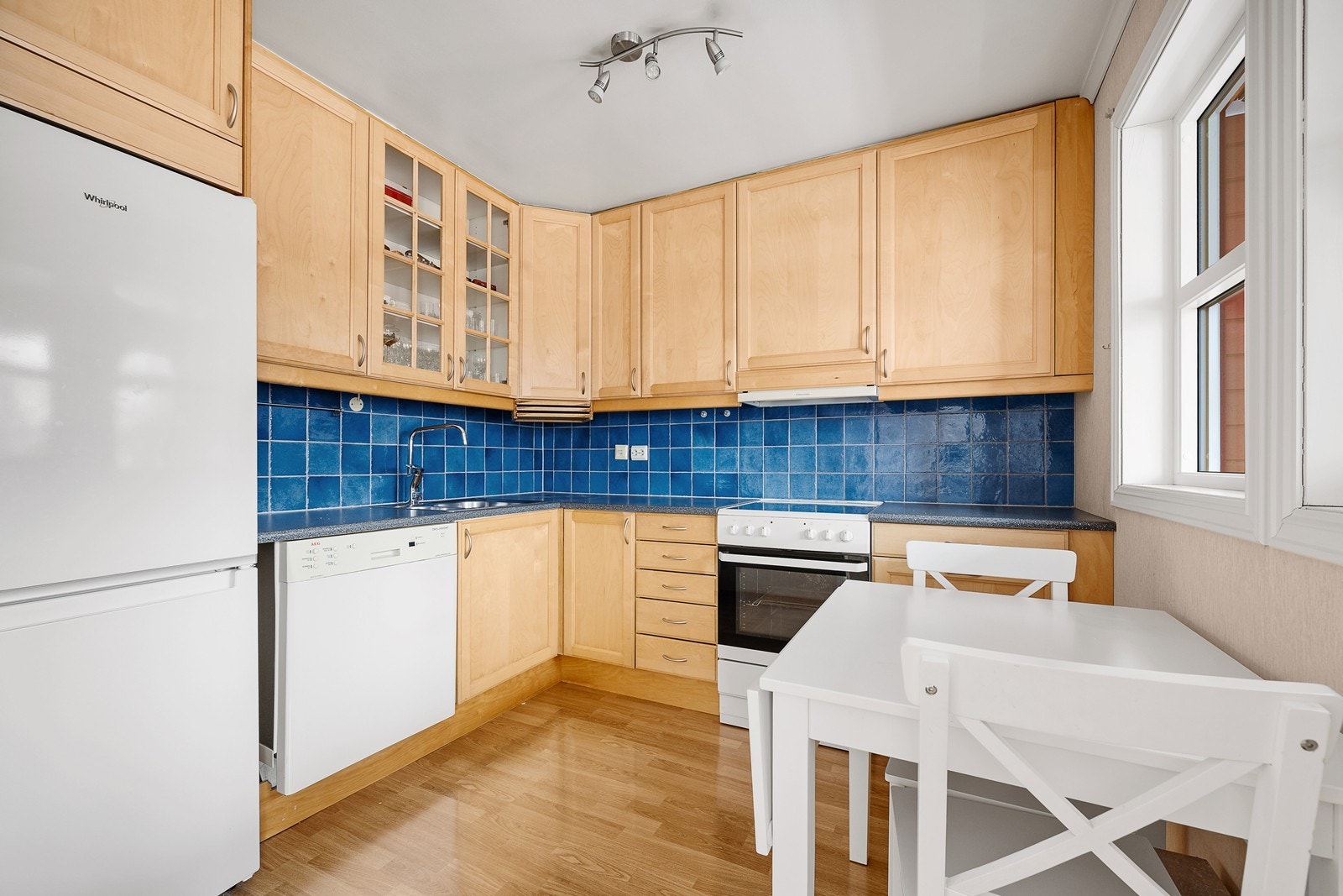 Pent kjøkken med mye lagringsplass og plass til frokostgruppe ved de to vinduene Galleribilde