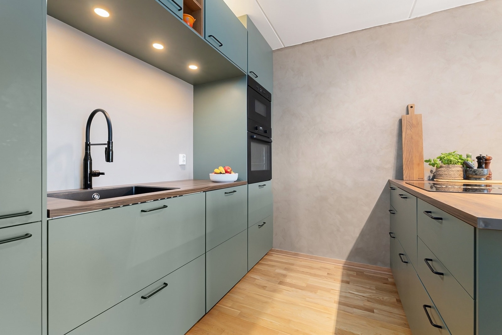 Innredning med grønne, glatte skapfronter, benkeplater i laminat, planlimt oppvaskkum og ett-greps armatur, begge i sort utførelse Galleribilde