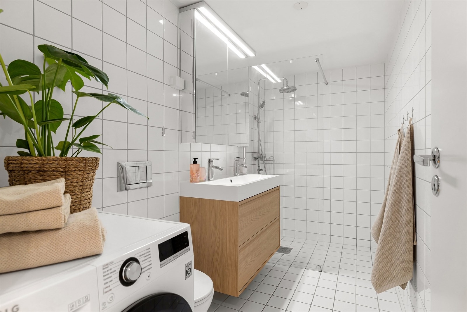 Delikat baderom med hvite vegg- og gulvfliser med varmekabler og opplegg for vaskemaskin Galleribilde