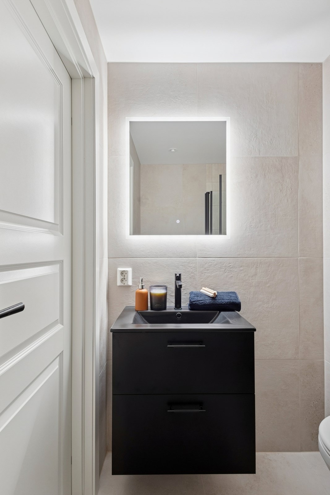 Servantinnredning med sorte glatte fronter, sort heldekkende servant, sort ettgreps servantarmatur og speil med led belysning. Galleribilde