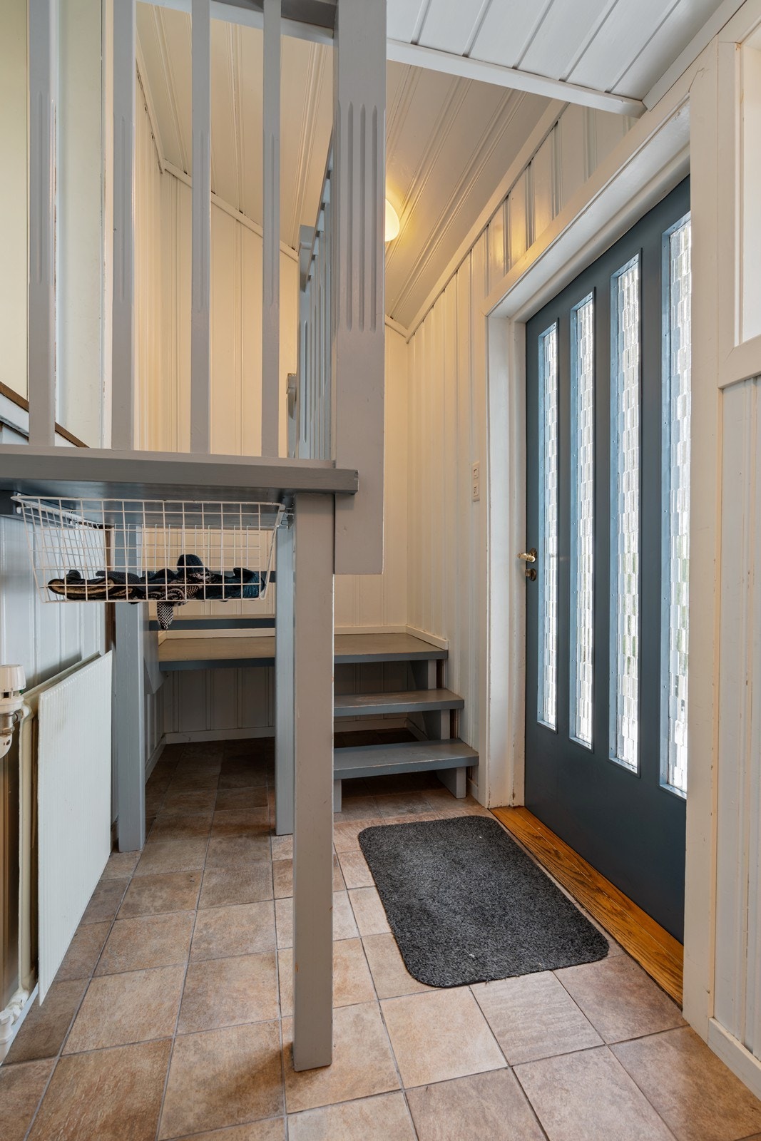 Entréen er plassert i et eget avlukke en halv etasje nedenfor 1. etasje, med praktisk flislagt gulv. Herfra leder trappen naturlig opp til første etasje, og rommet gir et hyggelig og funksjonelt førsteinntrykk av boligen. Galleribilde