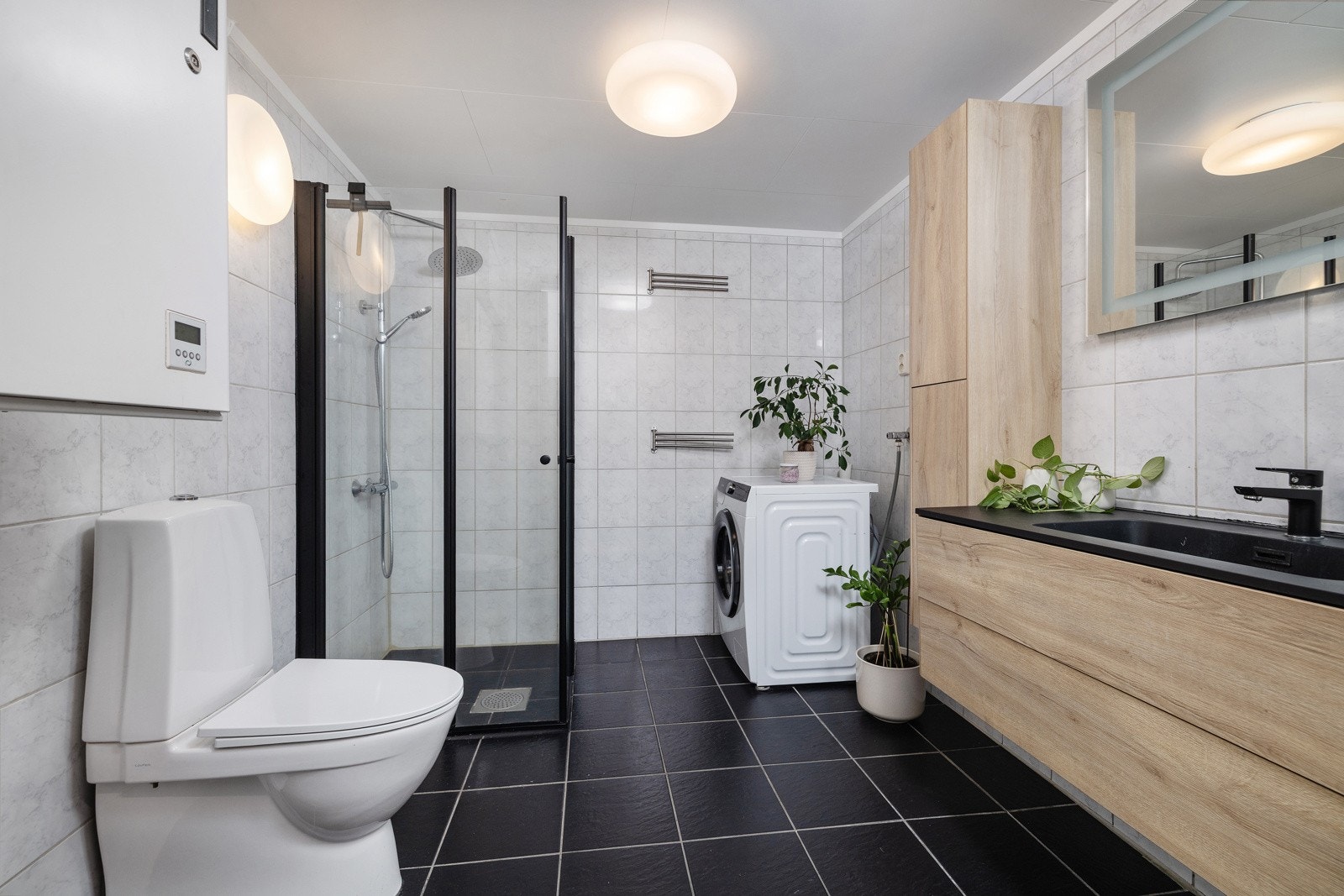 Flislagt baderom med varme i gulvet og opplegg for vaskemaskin. Regnfallsdusj i hjørnet. Galleribilde