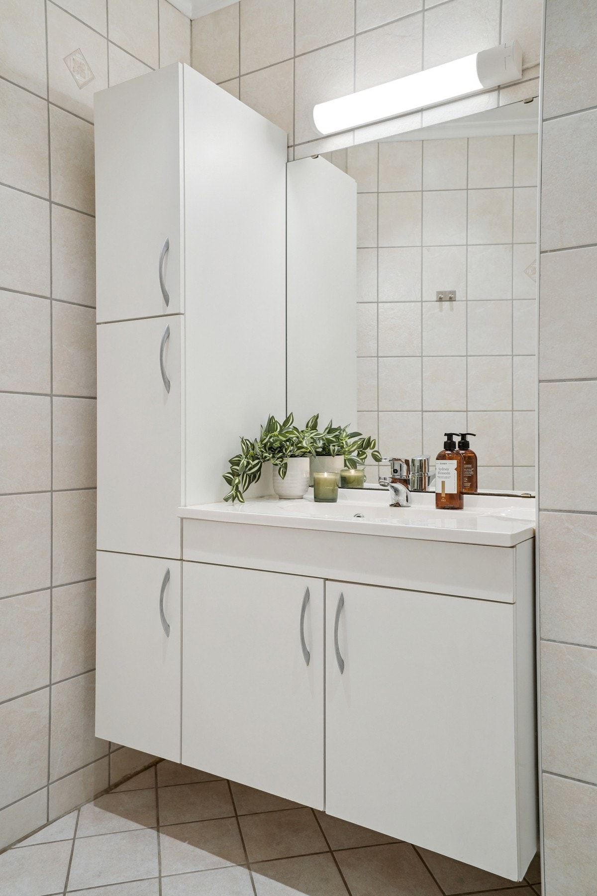 Baderomsinnredning med lyse glatte fronter og hvit helstøpt servant med speil og belysning over. Galleribilde