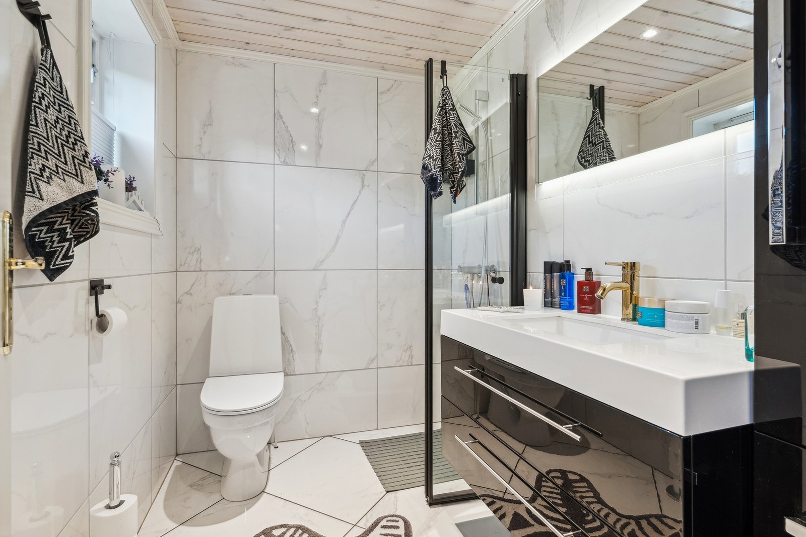 Delikat og fint bad med flislagte overflater. Dusjhjørne med med innfellbare glassvegger, baderomsinnredning med helstøpt servantplate og gulvmontert toalett. Galleribilde