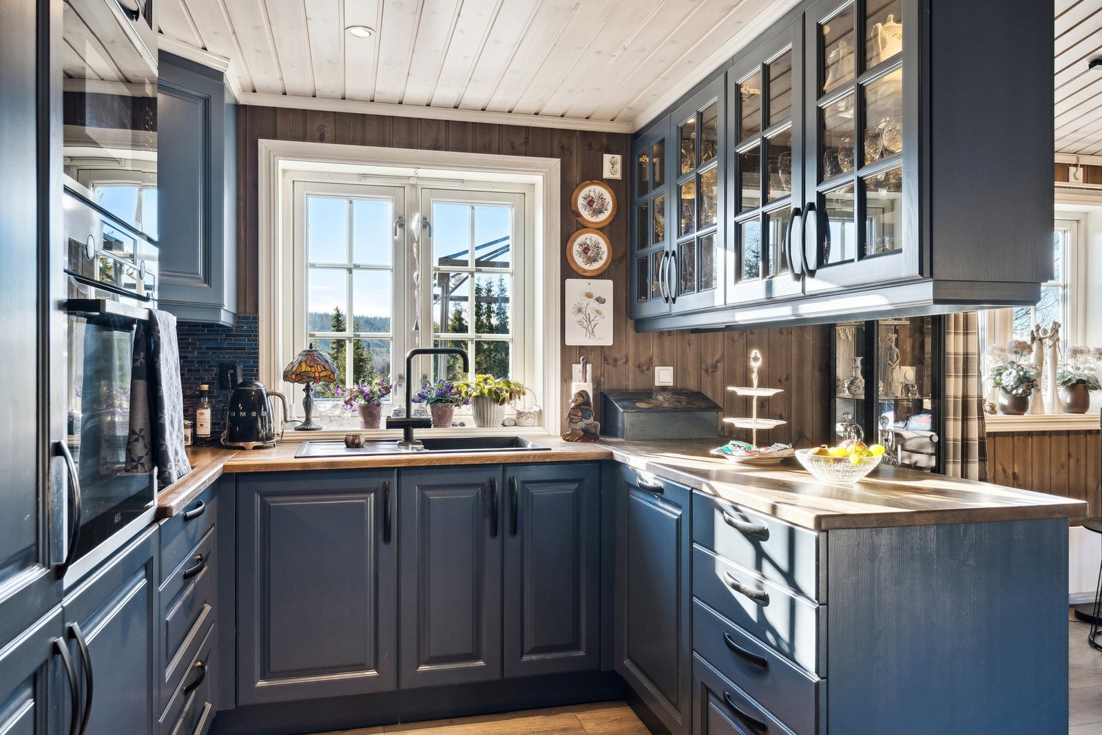 Kjøkkenet ligger i naturlig tilknytning til stuen. Kjøkkeninnredning av heltre med profilerte fronter, malt i en fin blåfarge. Benkeplate av heltre eik, med kjøkkenbar mot stuen. Galleribilde