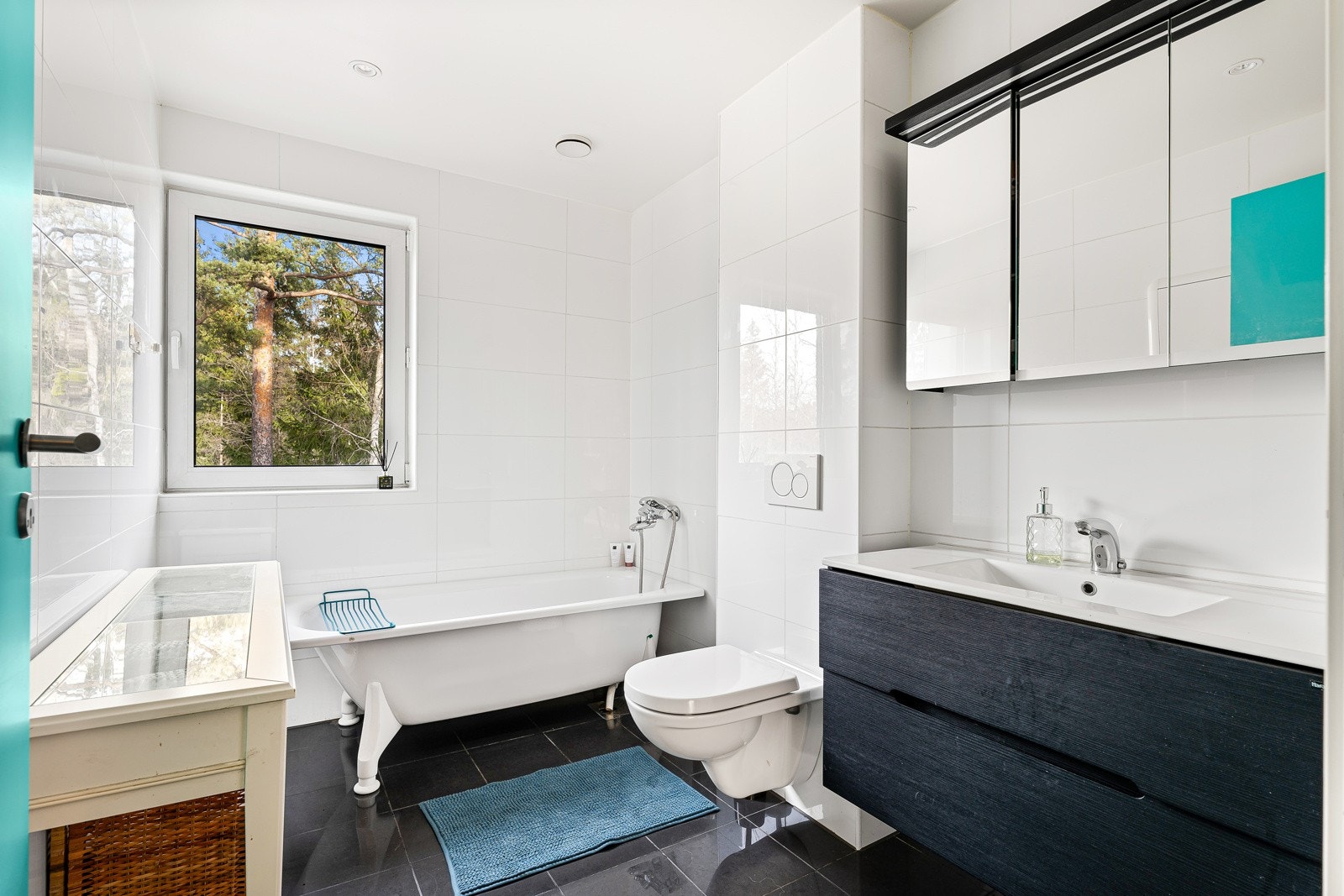 Bad med fliser på vegger og gulv, stilrent interiør med badekar, servantinnredning og vegghengt toalett. Galleribilde