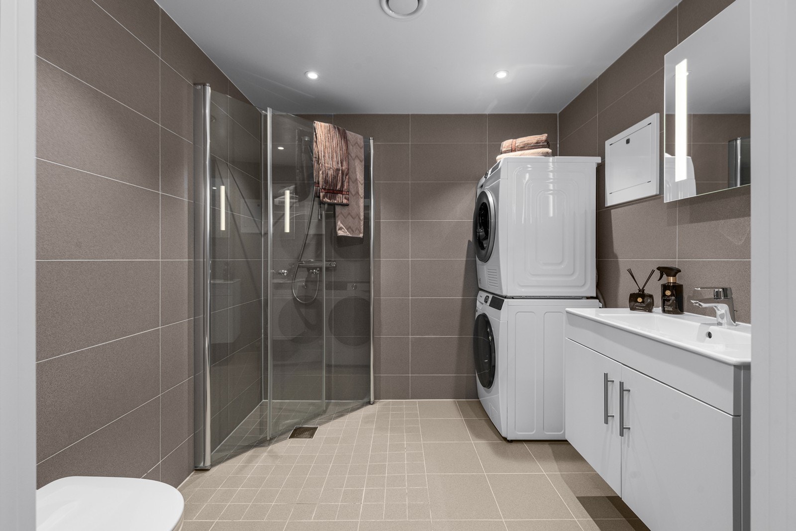 Moderne flislagt baderom med klassiske og tidløse flisvalg, vegghengt wc, helservant på baderomsinnredning og praktisk innfellbare dusjvegger i herdet glass. Galleribilde