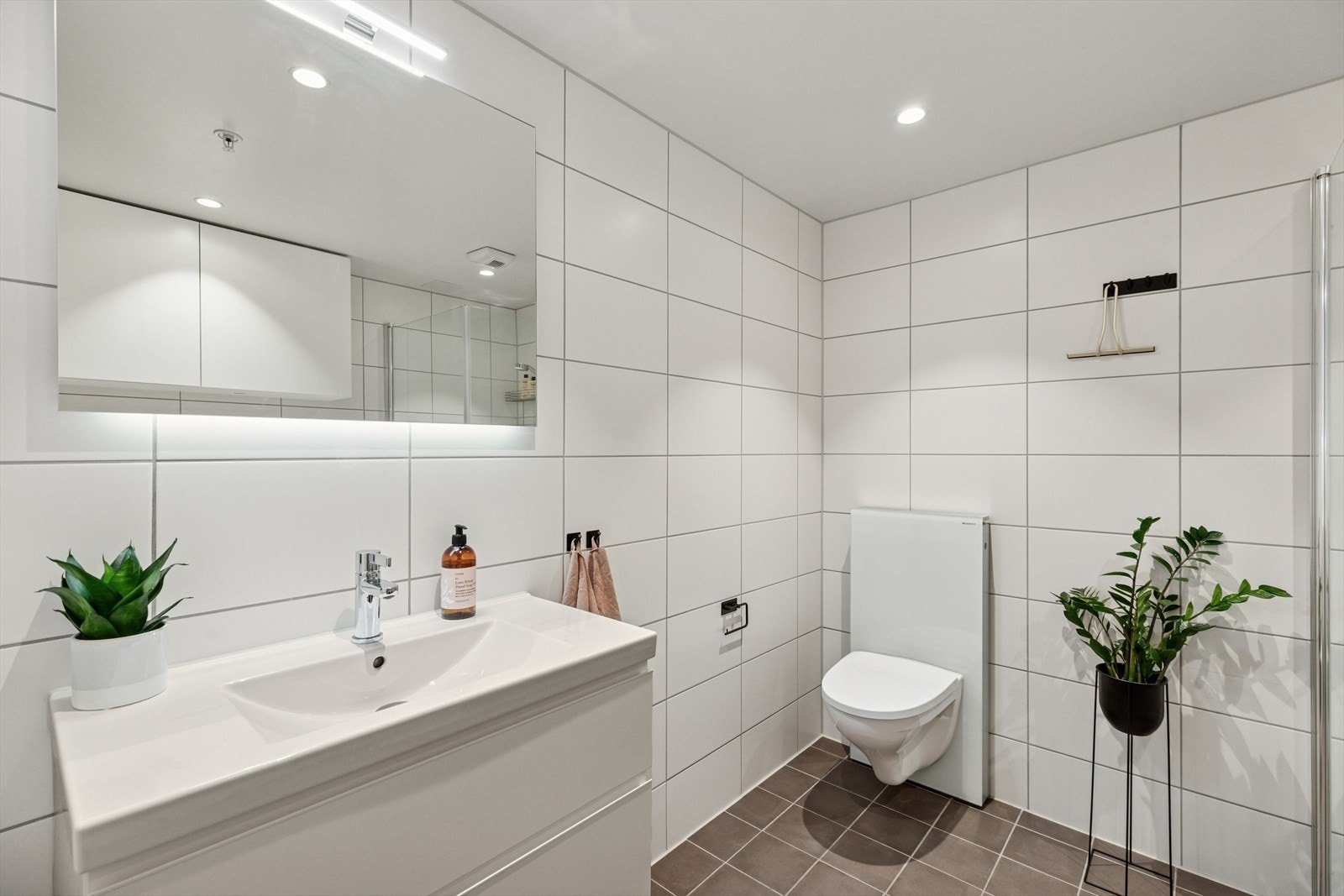 Begge badene er utstyrt med vegghengt toalett, servantinnredning og dusjhjørne med innfellbare glassdører. Galleribilde