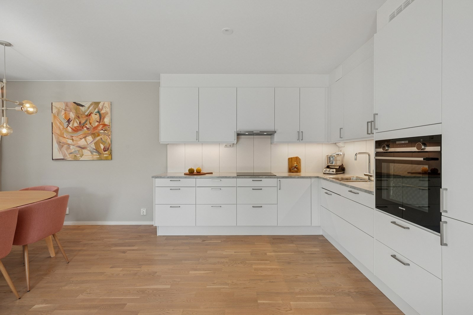 Kjøkkeninnredningen er pen og tidløs, med hvite, glatte fronter, laminat benkeplate og underlimt vask i rustfritt stål. Galleribilde