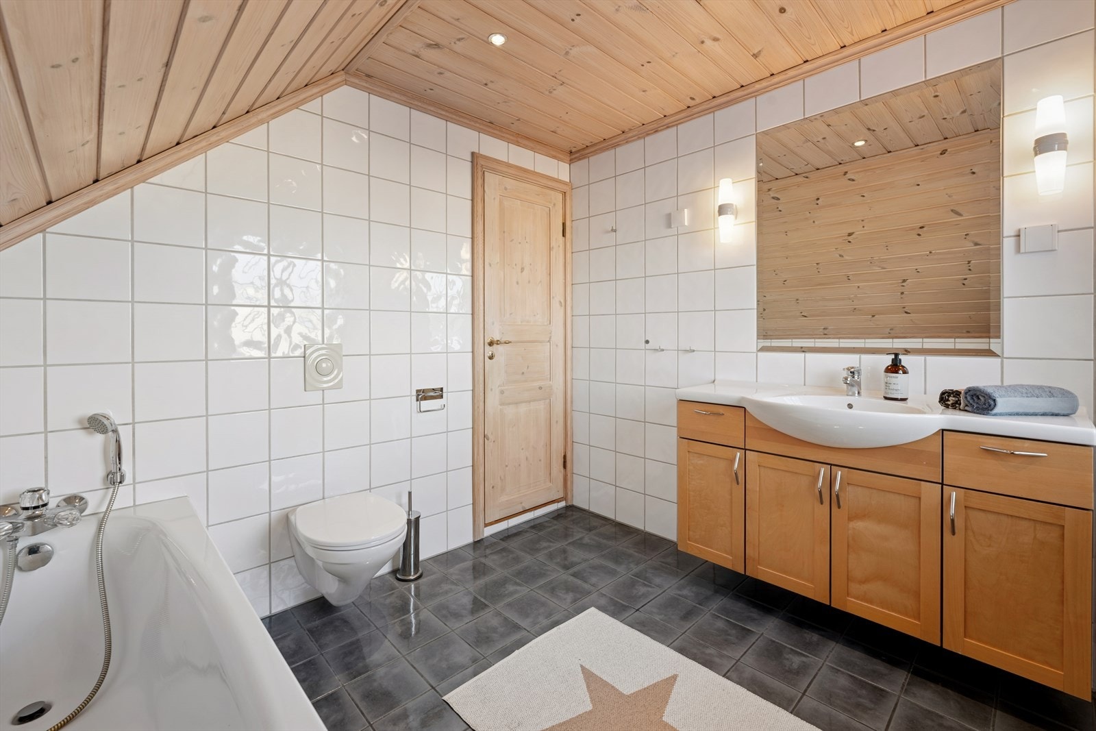 Baderom i 2. etasje med flislagte vegger og gulv som er innredet med servant med skap, vegghengt toalett og badekar. Galleribilde