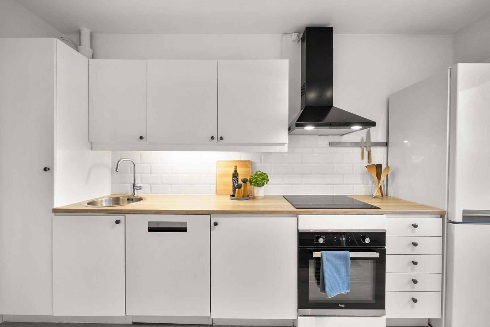 Det er laminat benkeplate med nedfelt vaskekum, samt fliser og belysning over benkeplaten. Galleribilde