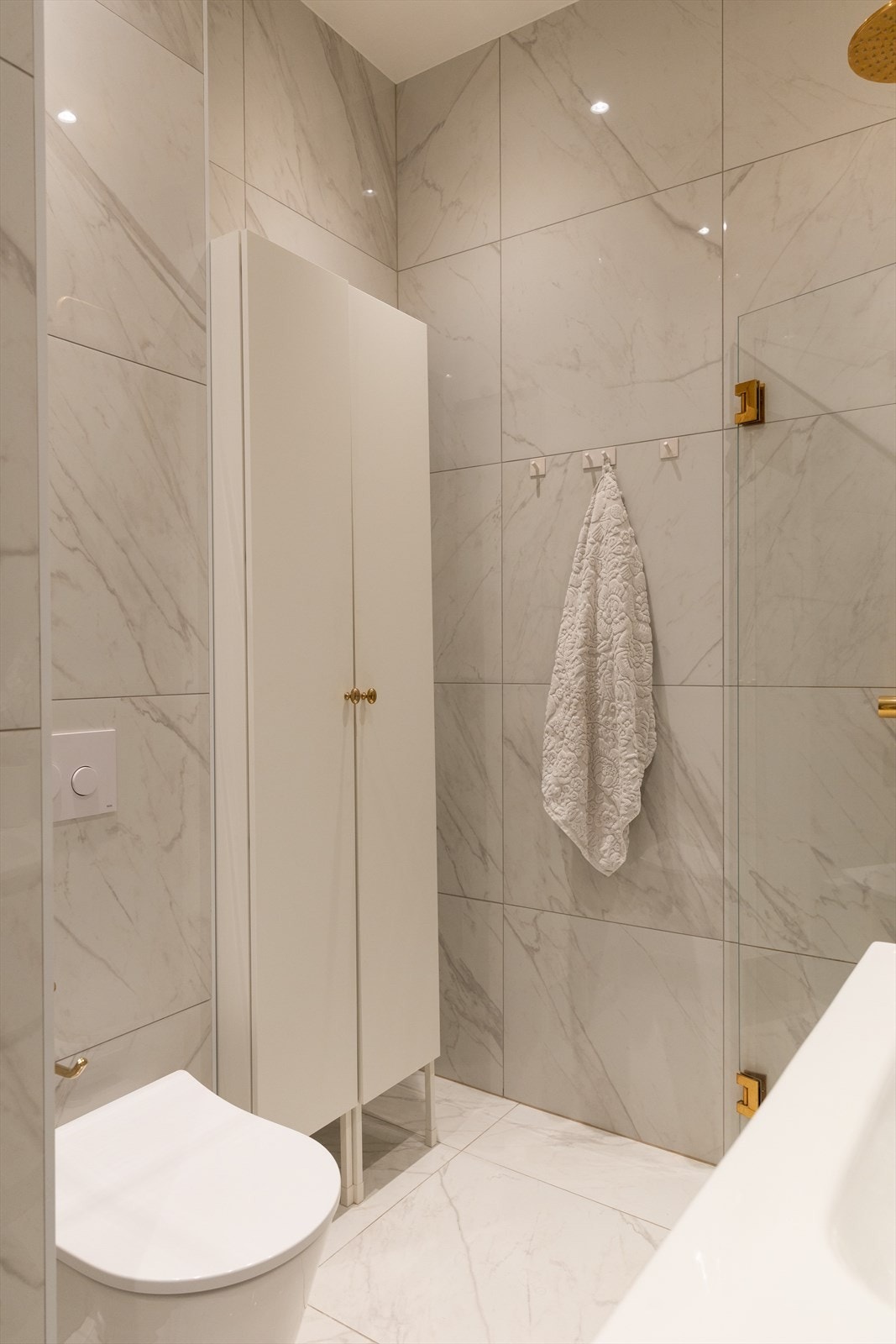 Badet er innredet med servant med underskuffer, vegghengt toalett med skjult sisterne og dusjhjørne med blandebatteri i messing, hånddusj og regnfallshode. Galleribilde