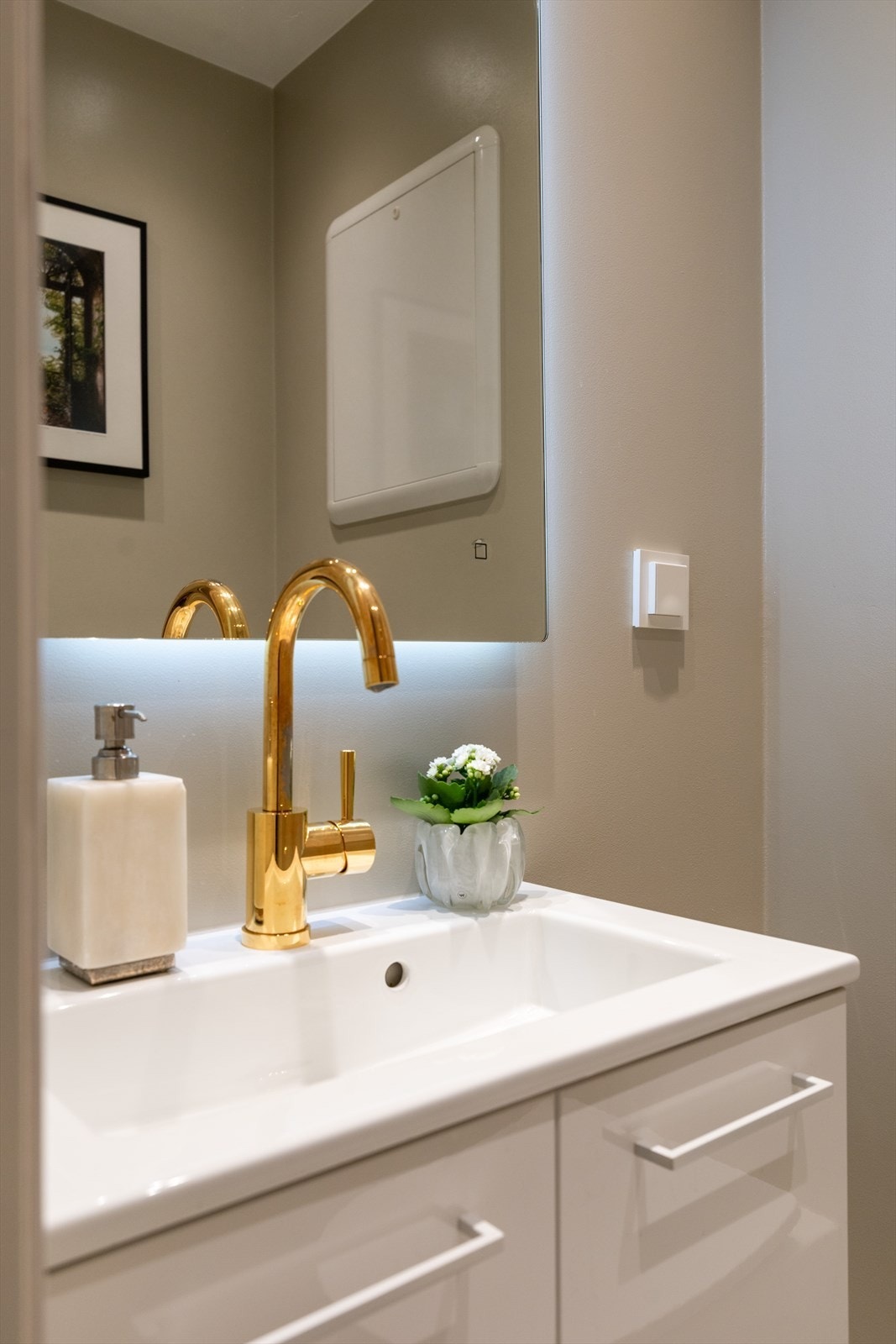 Innredet med servant med underskap, speil med integrert belysning og vegghengt toalett med skjult sisterne. Galleribilde