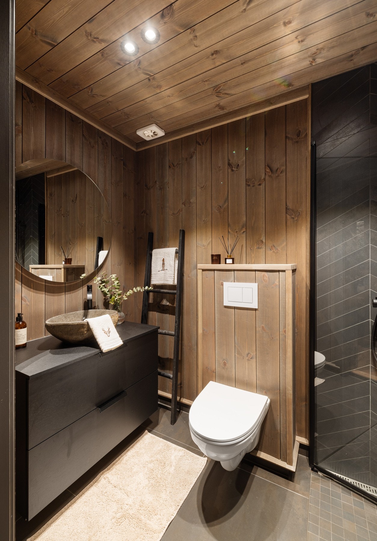 Begge bad har sort innredning med skuffer, bollevask, rundt speil, dusjhjørne med fliser i fiskebeinsmønster samt vegghengt toalett Galleribilde