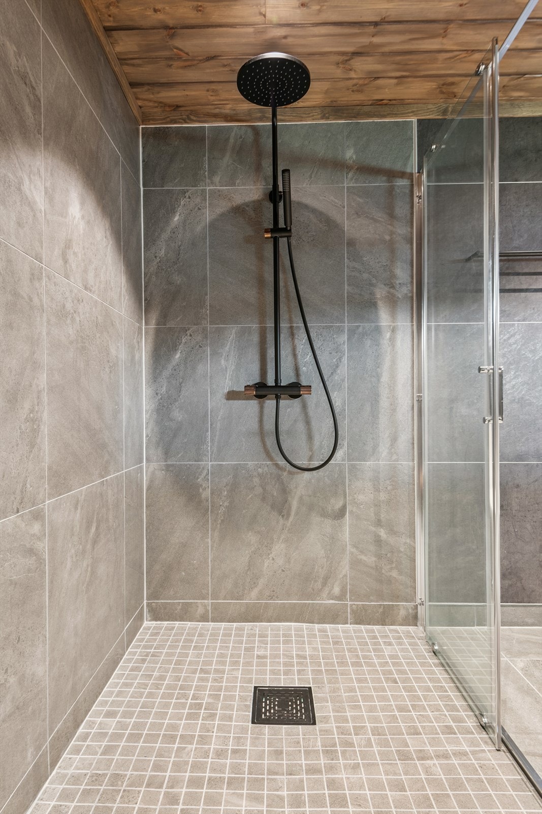 Flislagt dusjsone med moderne, sorte armaturer og mosaikkfliser i gulvet Galleribilde