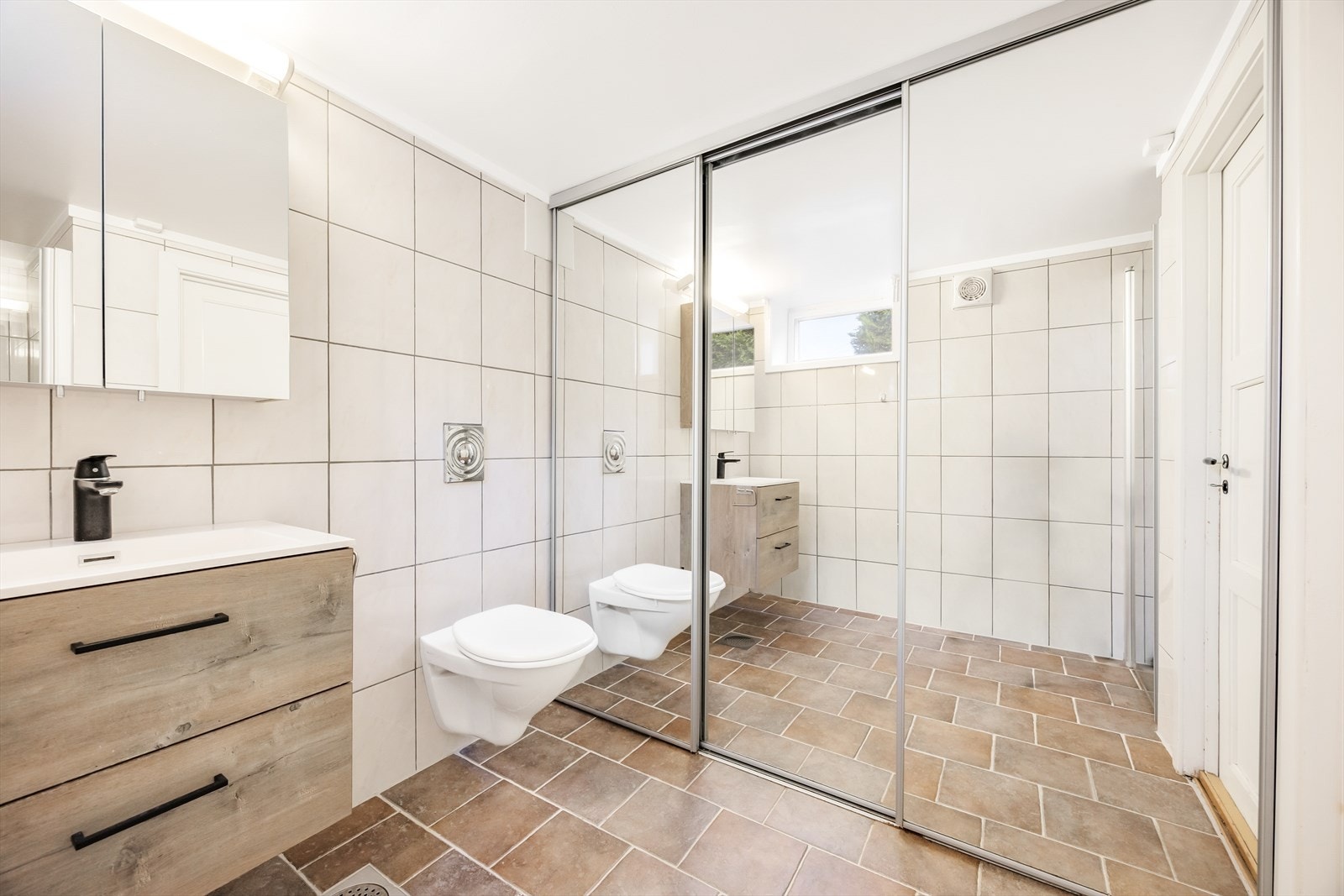 Badet er utstyrt med dusjnisje med innfellbar glassdør, vegghengt wc og servantinnredning med skuffer og overskap Galleribilde