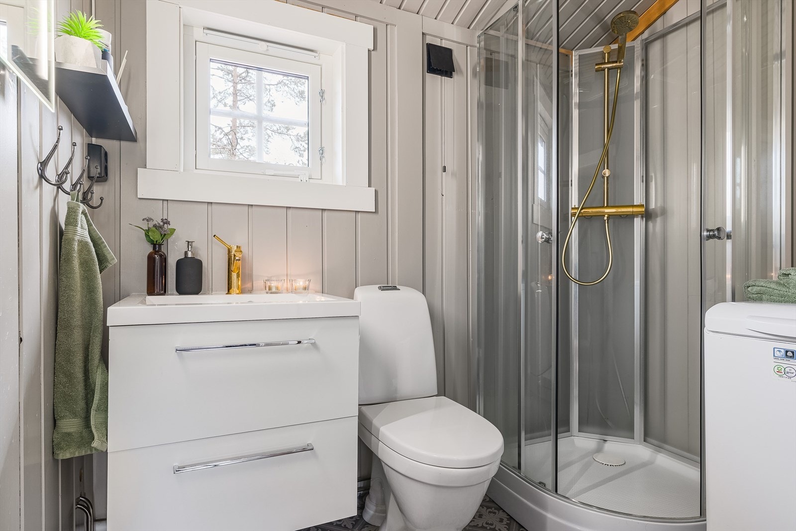 Pent baderom med dusjkabinett, servant på innredning, toalett og opplegg for vaskemaskin. Galleribilde