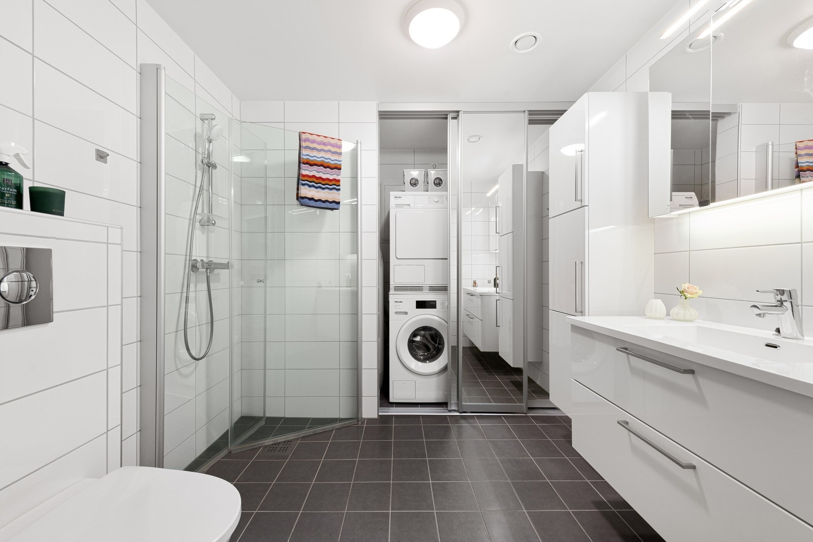 Flislagt bad med varmekabler i gulv. Det er skyvedørsfronter med speildører som skjuler varmtvannsbereder, stoppekran, opplegg for vaskemaskin og ventilasjonsaggregat. Galleribilde