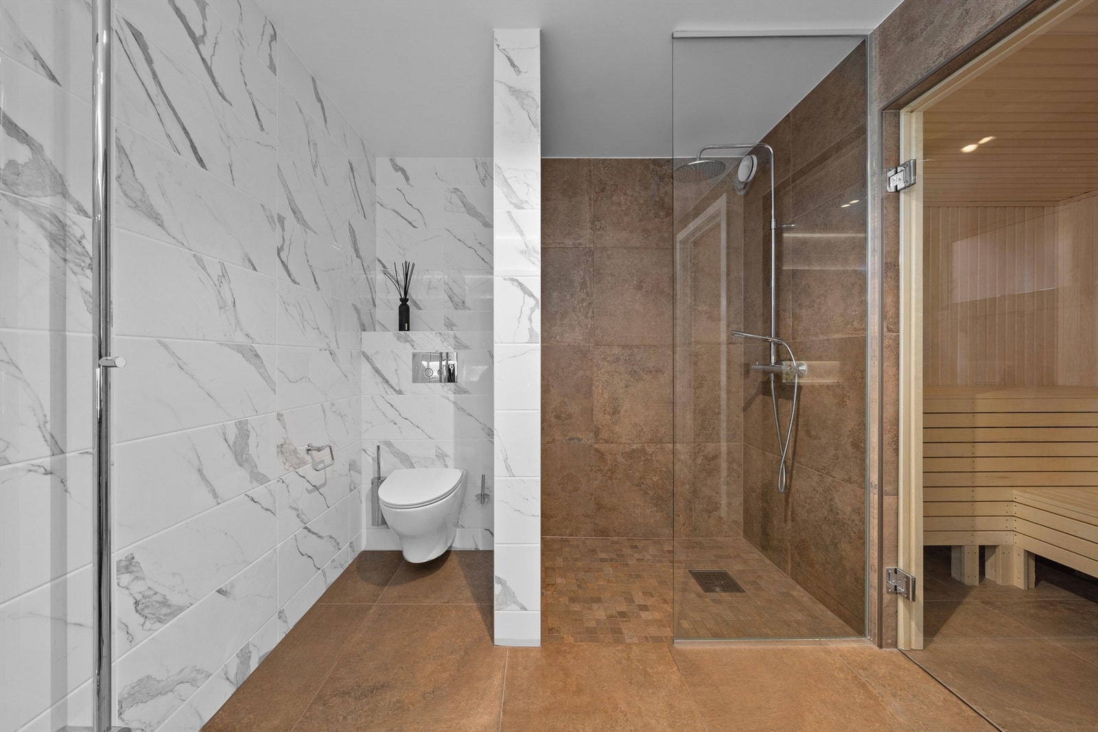 Dusjnisje med glassvegg, flislagt vegg med innebygd dusjhylle, og mosaikkfliser på gulv. Vegghengt toalett. Galleribilde