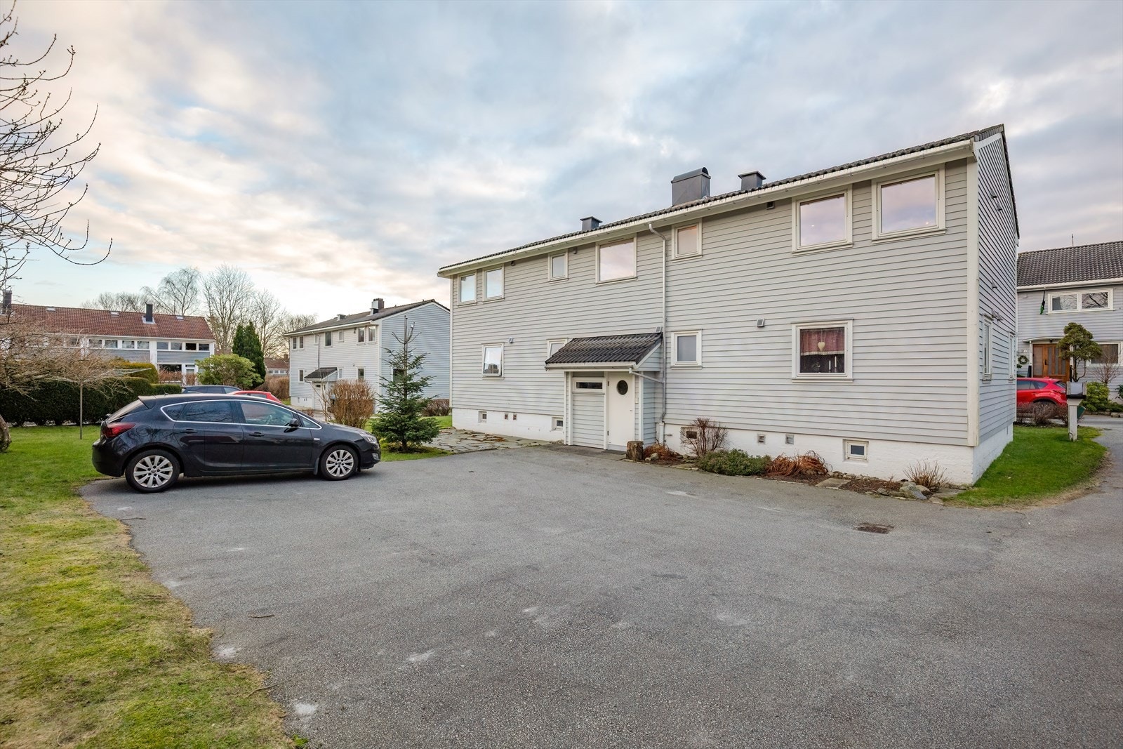 Fasade ved inngangspartiet. Stor utvendig biloppstillingsplass som tilhører borettslaget. Galleribilde