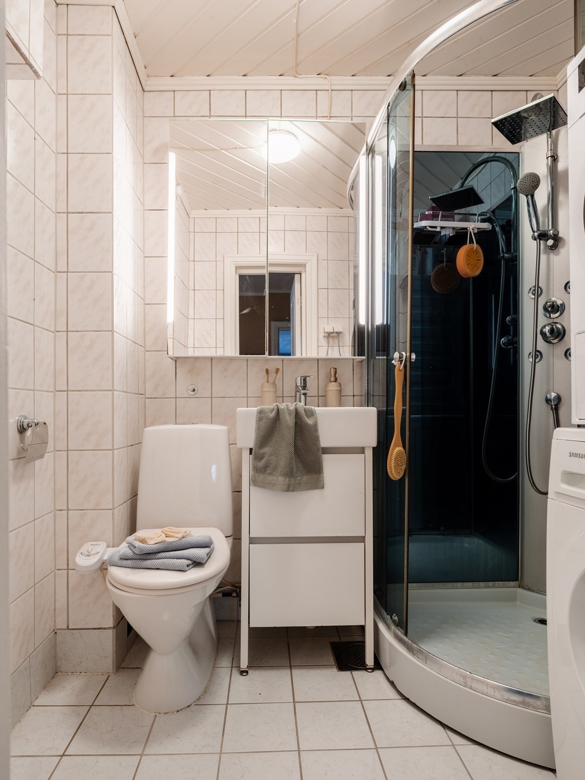 Et lyst, flislagt baderom med varme i gulvet og opplegg for vaskemaskin/tørketrommel. Galleribilde