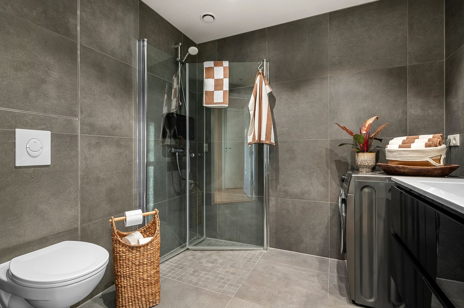 Flott, flislagt bad med opplegg for vaskemaskin og veggfestet toalett i moderne farger Galleribilde