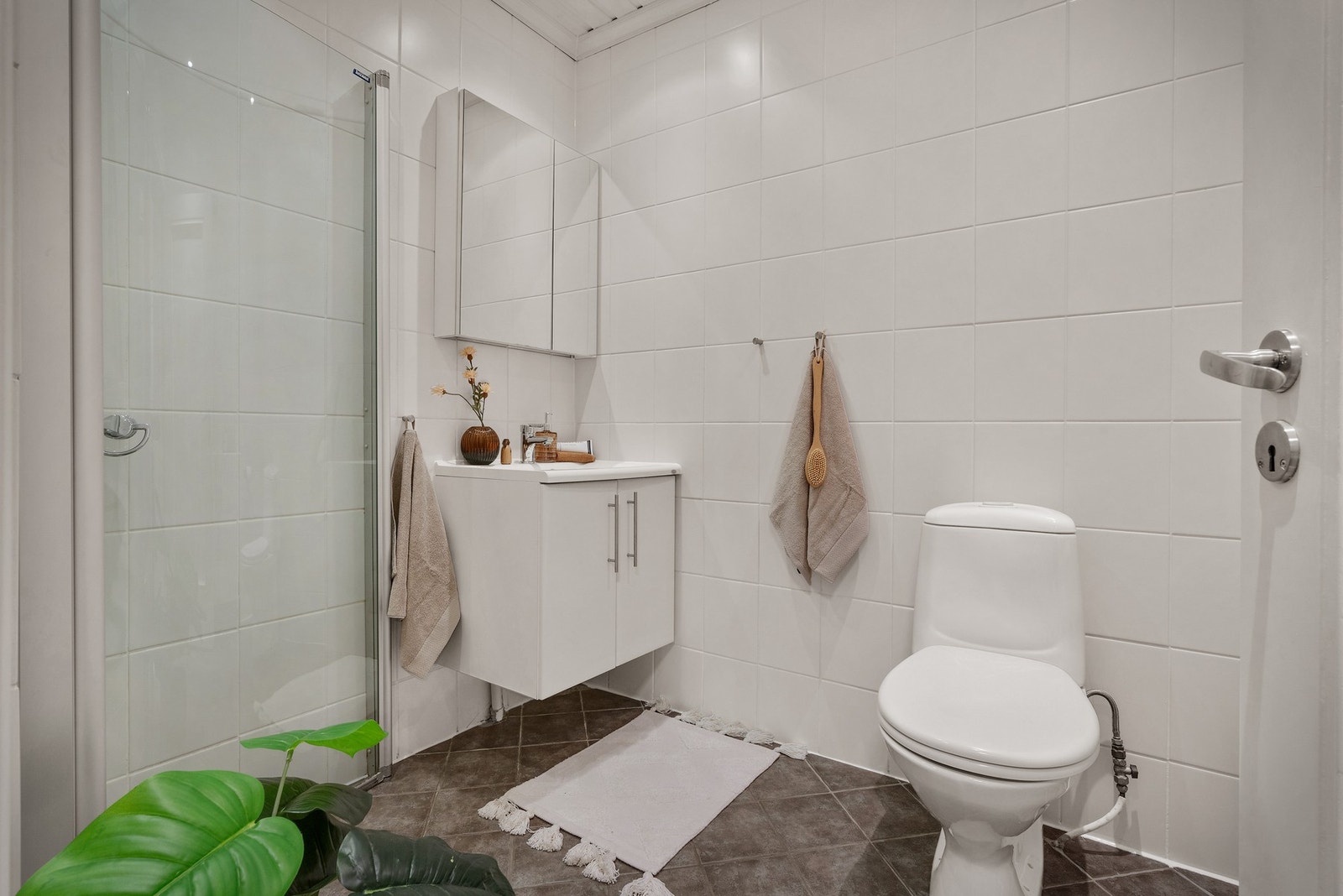 - Badet er lyst og klassisk med fliser på gulv og vegger, og inneholder toalett, servant med skap og dusjdører i glass - Galleribilde