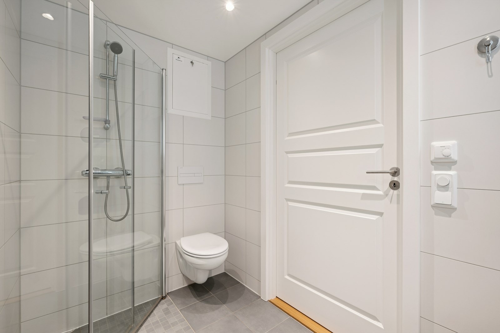 Badet har flislagte vegger og gulv, og er innredet med nedfelt servant, veggmontert toalett, dusjhjørne og opplegg for vaskemaskin. Galleribilde