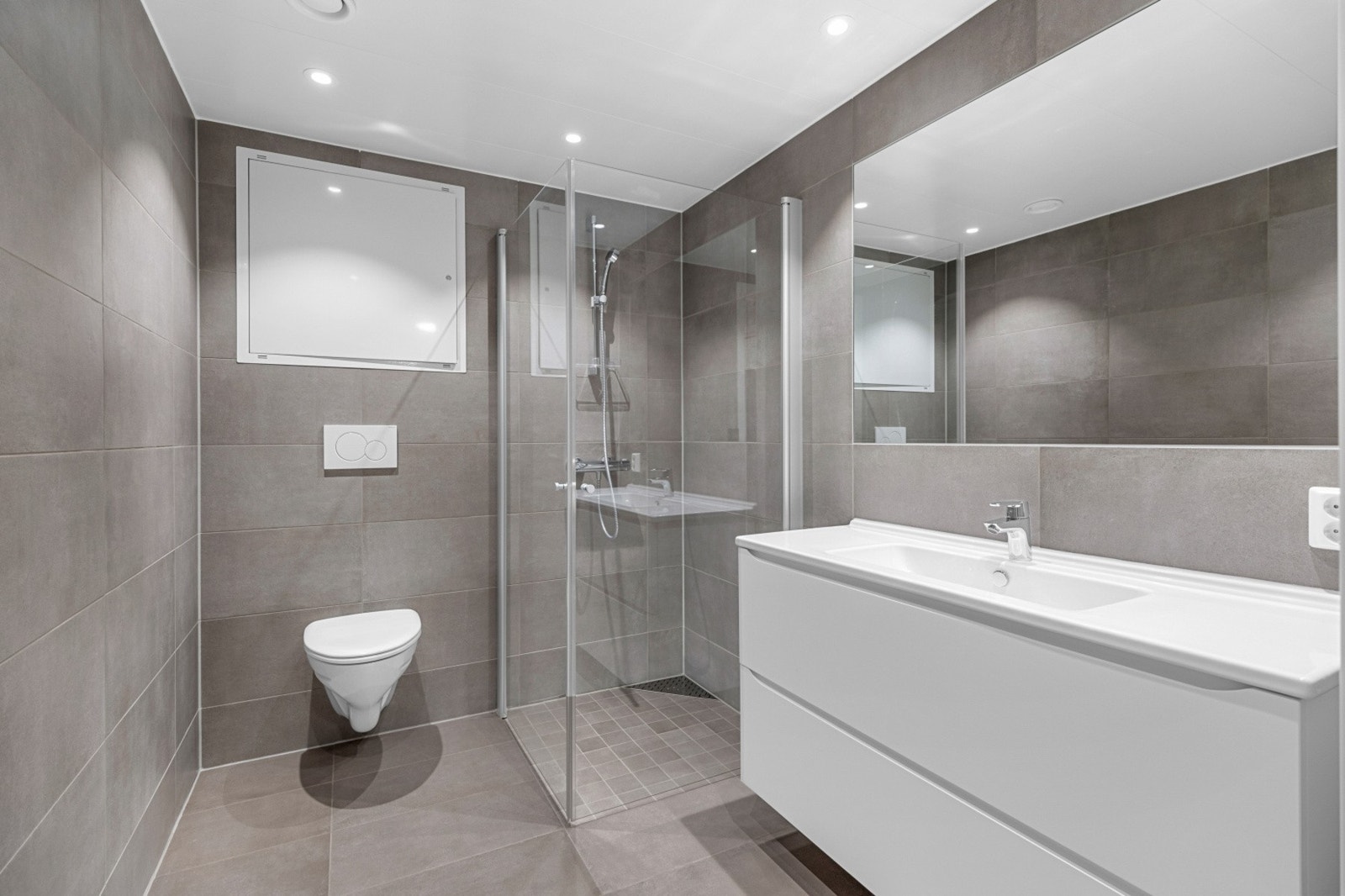 Stilig og flislagt bad med gulvvarme, vegghengt wc, servant med speil og dusjhjørne. Galleribilde