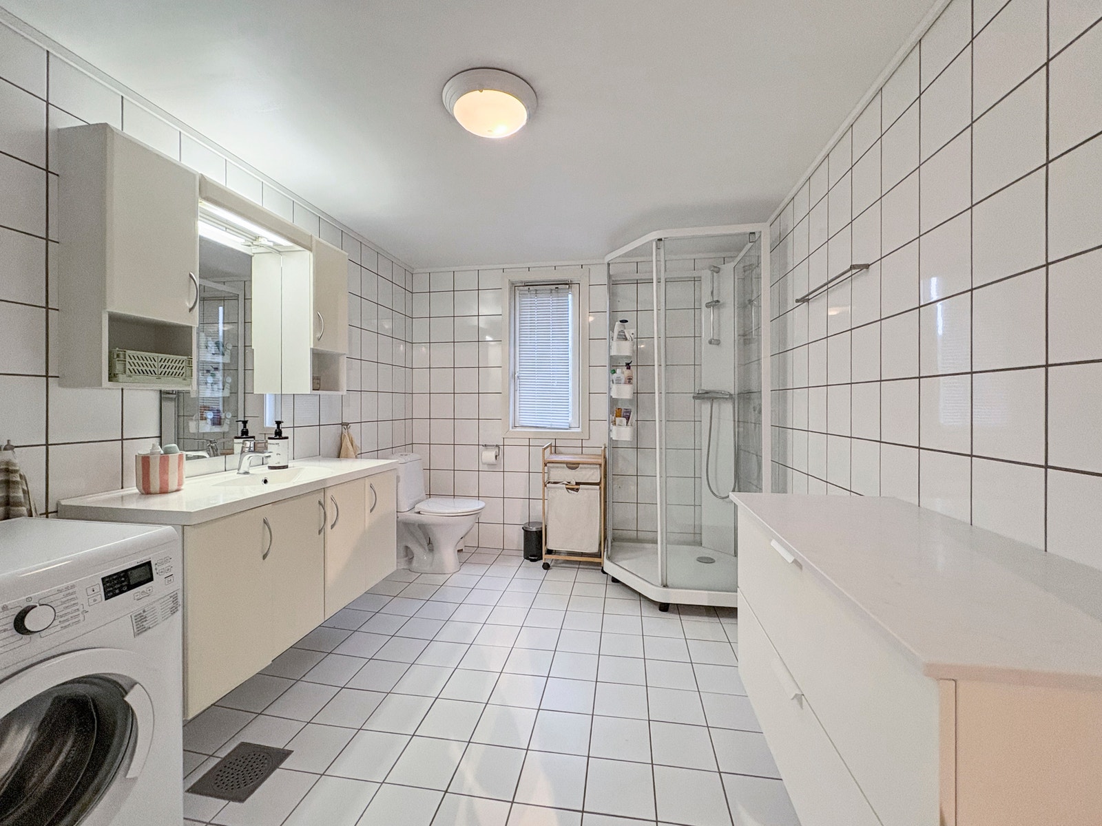 Stort flislagt bad med praktiske oppbevaringsmøbler. Galleribilde