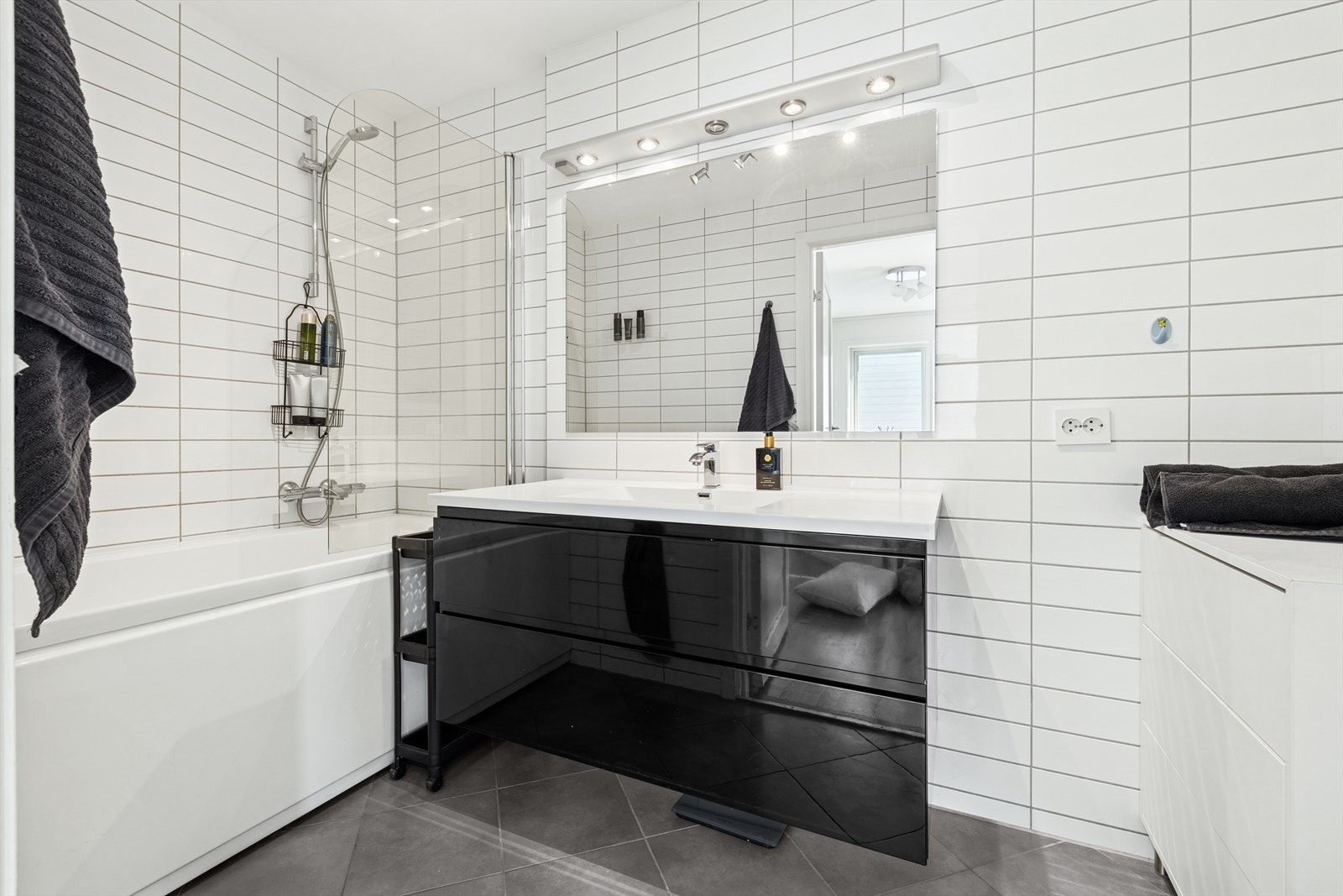 Badet har flislagt gulv, badekar med dusj-garnityr og baderoms seksjon med ekstra oppbevaringsplass. Galleribilde