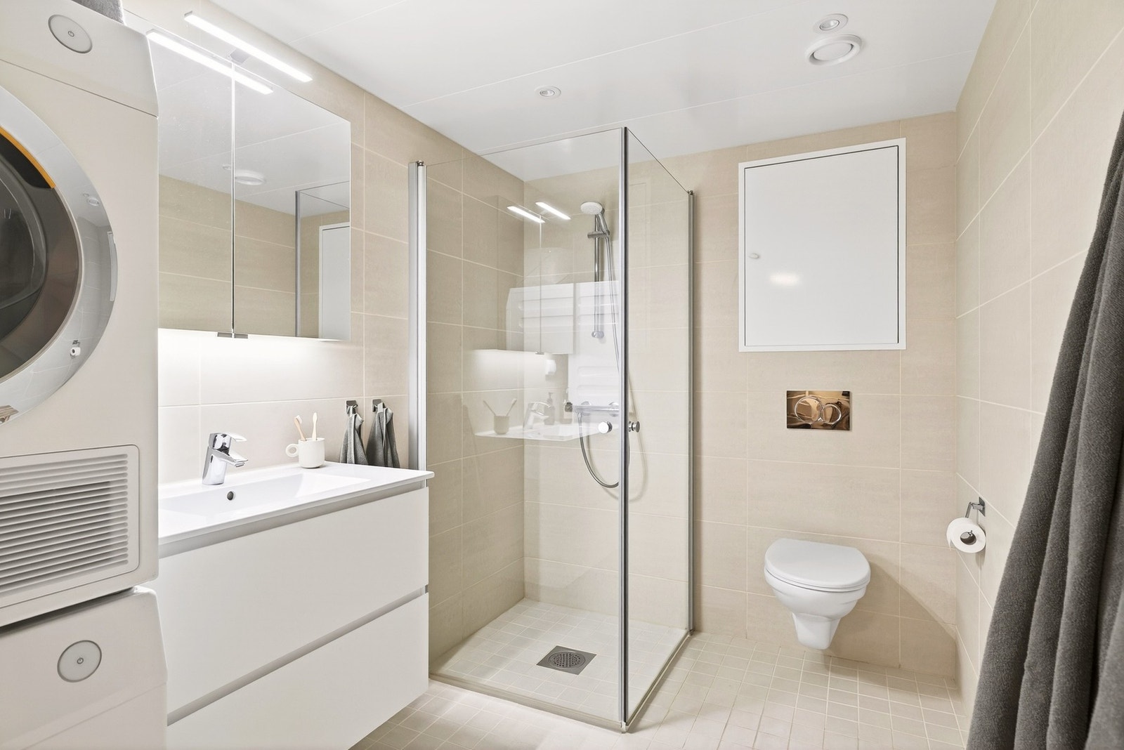 Badet har en stilren baderomsinnredning med underskuffer, speilskap med lys og opplegg for vaskemaskin. Galleribilde