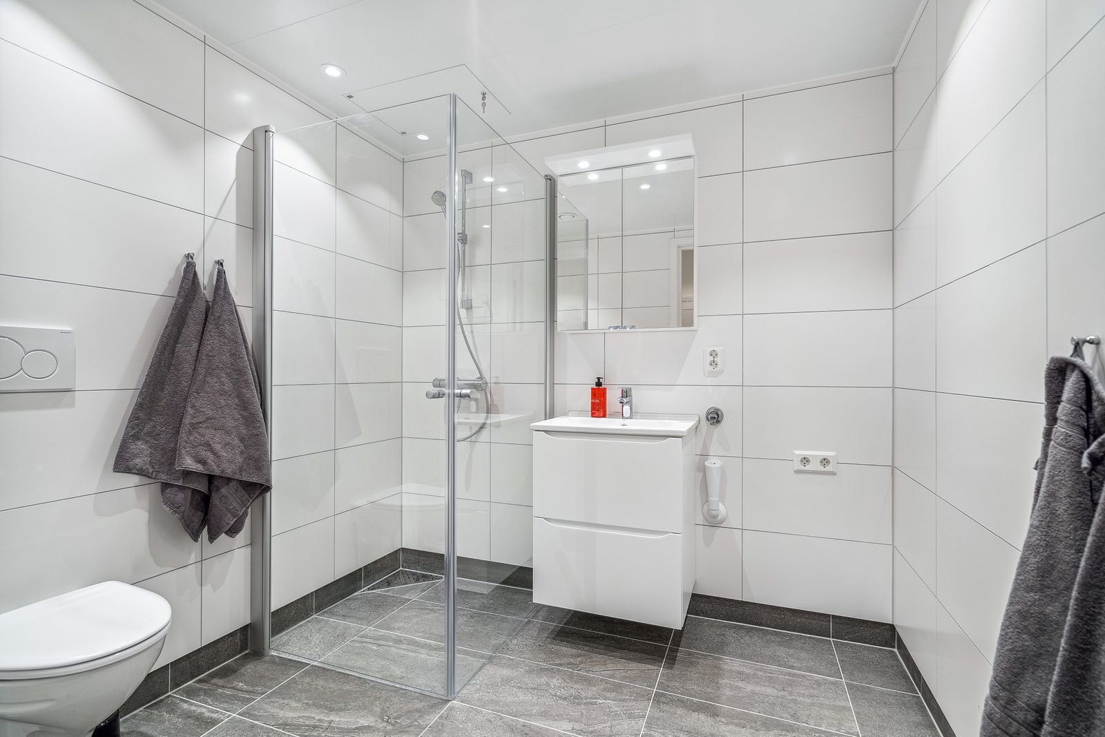 Lyst og komplett flislagt bad, med stor hjørnedusj.