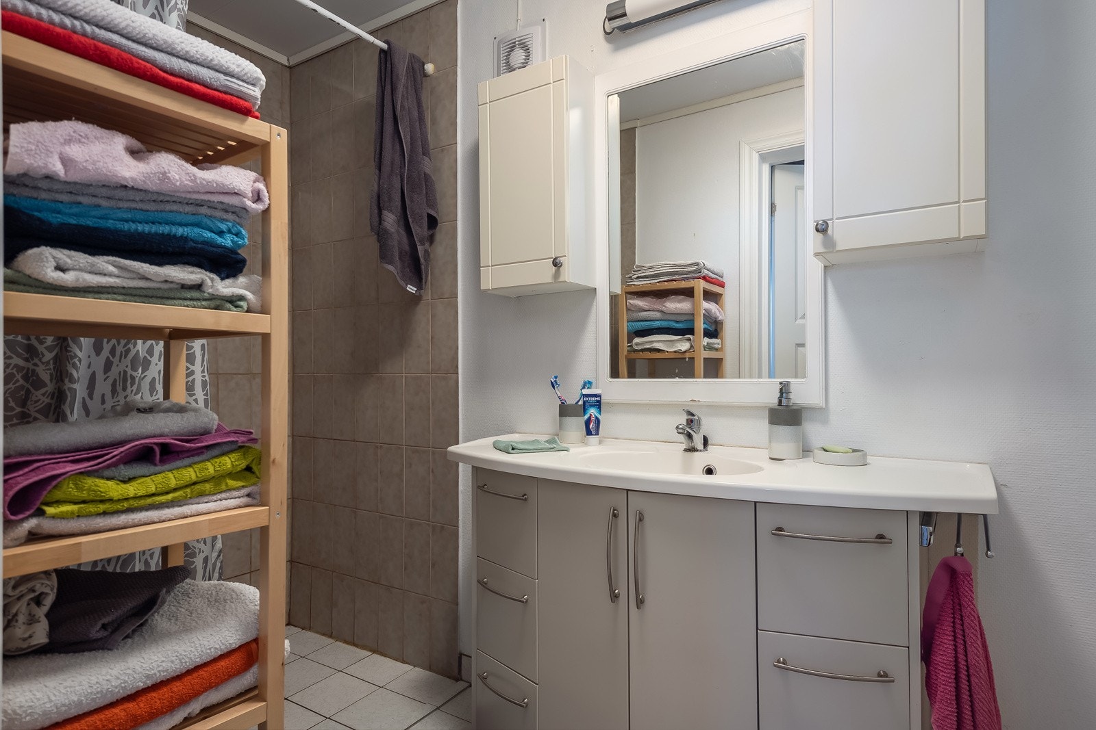 Bad med flislagt gulv og varmekabler. Badet er innredet med servant med underskap, gulvstående toalett, opplegg for vaskemaskin, samt dusjgarnityr på vegg. Galleribilde