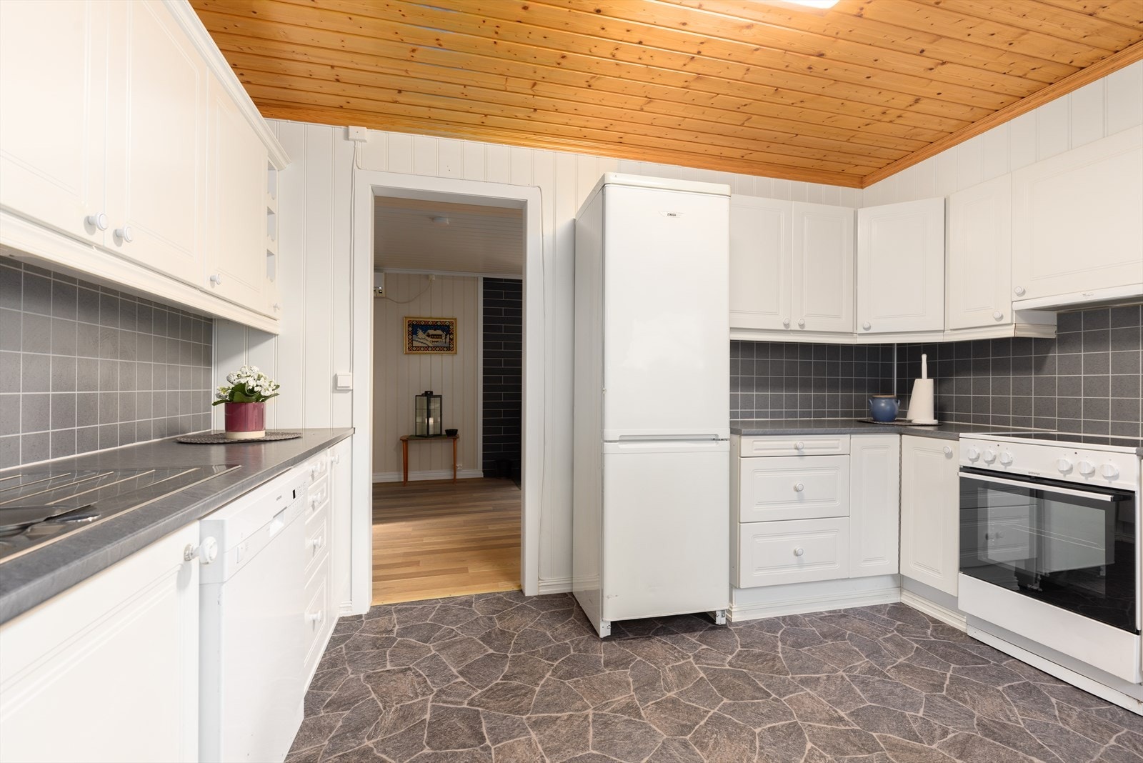 Kjøkkenet har en hvit innredning med profilerte fronter og noe glasskap, laminert benkeplate og beskyttelsesplater over kjøkkenbenk. Galleribilde