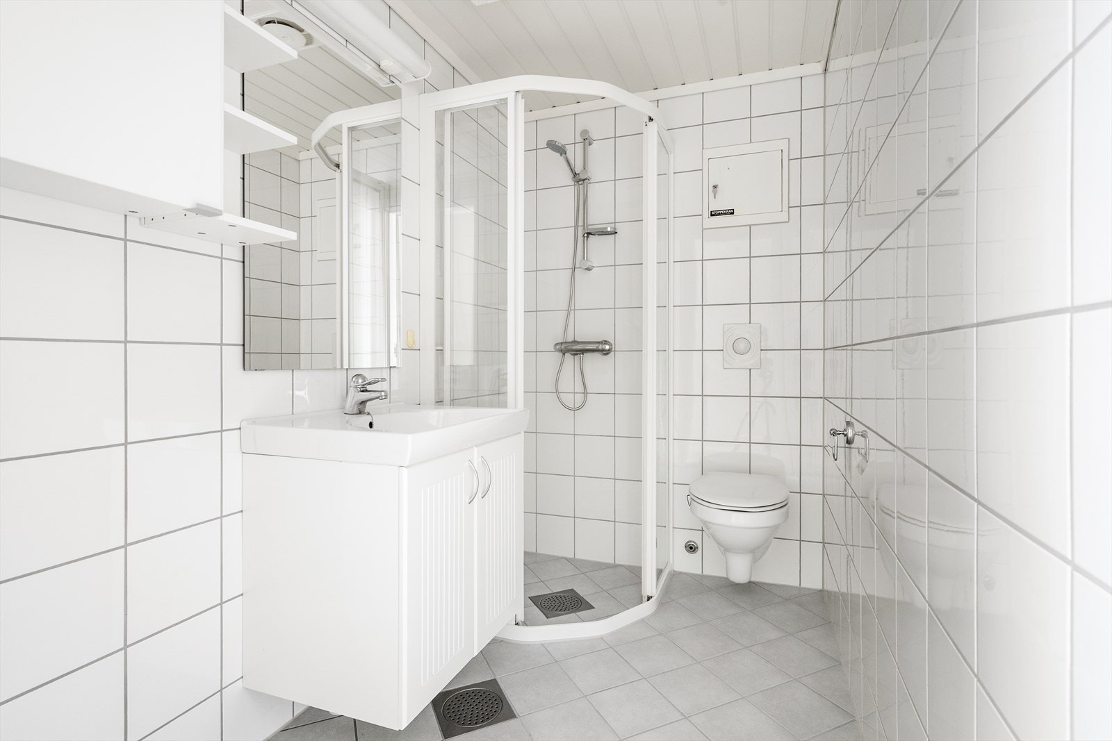 Lyst, flislagt bad pusset opp i regi av borettslaget i 2008. Badet har varmekabler, vegghengt toalett og servantinnredning, dusjhjørne og opplegg for vaskemaskin. Galleribilde