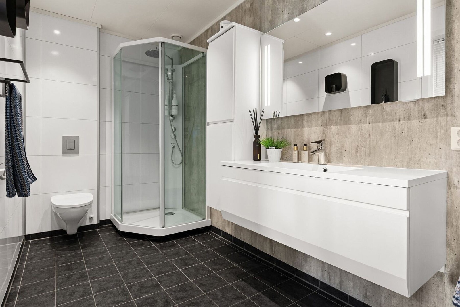 Stilrent bad innredet med vegghengt toalett, dusjkabinett og god oppevaringsplass ved vasken. Galleribilde