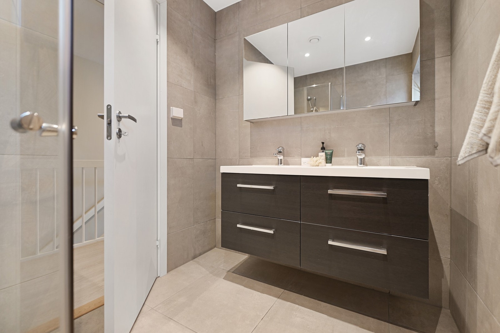 Delikat baderom med fliser på gulv og vegger. Moderne innredning med dobbel servant. Galleribilde