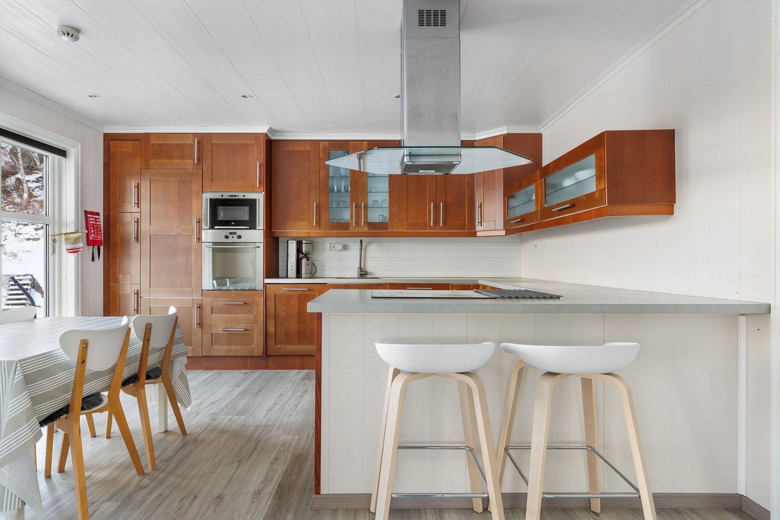 Romslig kjøkken med god plass til spisebord. Lys benkeplate og fronter i varm tone gir et elegant uttrykk. Praktisk barløsning. Galleribilde